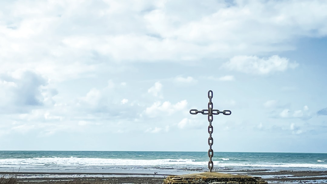 Cross made of chains on a beach with ocean waves.